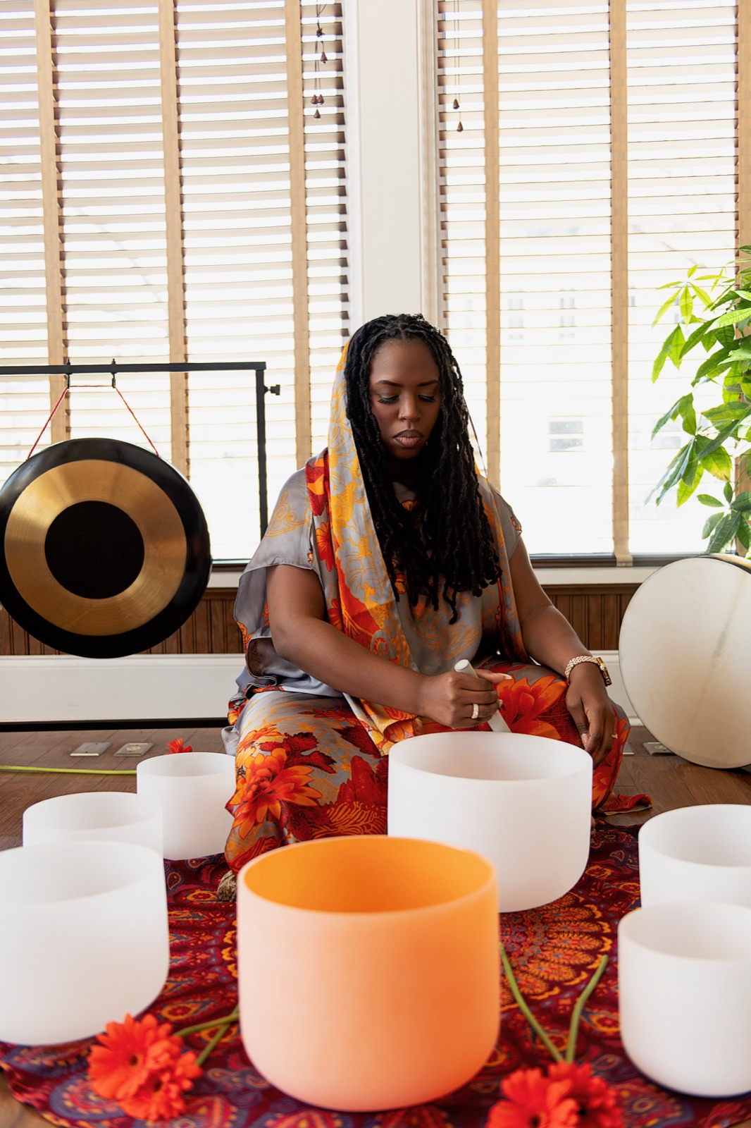 Keyona McCarthy kneeling at a circle of crystal singing bowls with a gong behind her