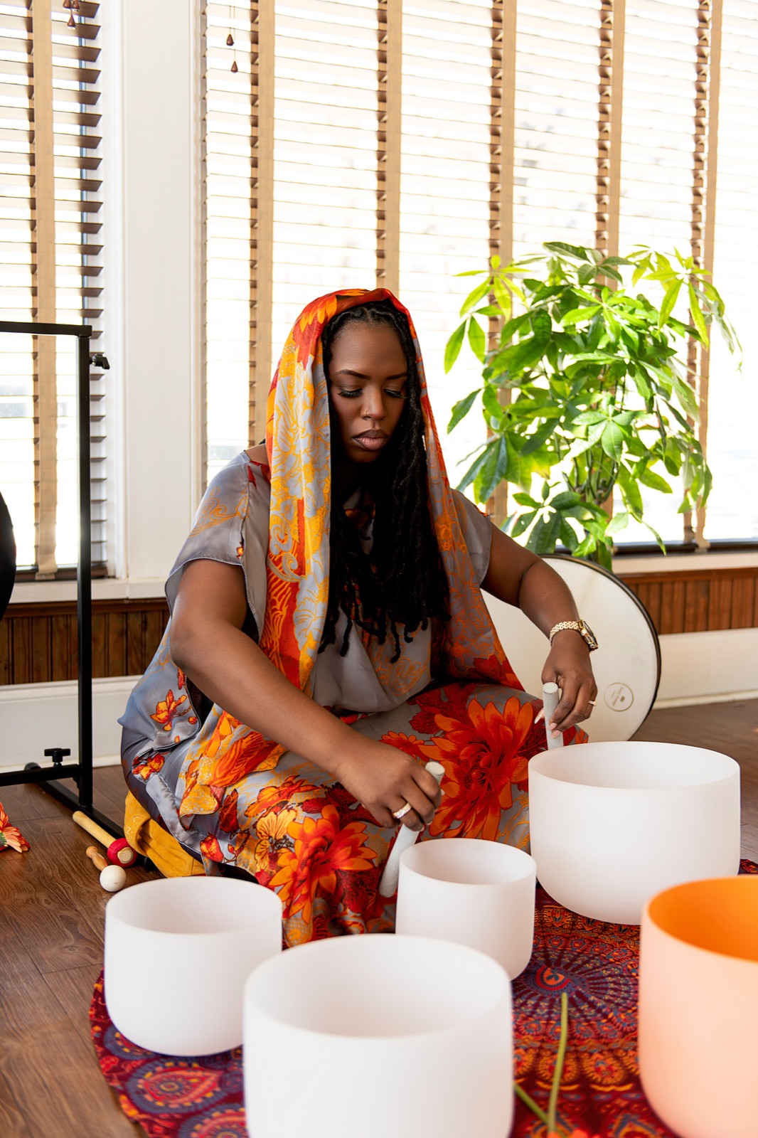 Keyona playing crystal singing bowls beside a gong and green plant